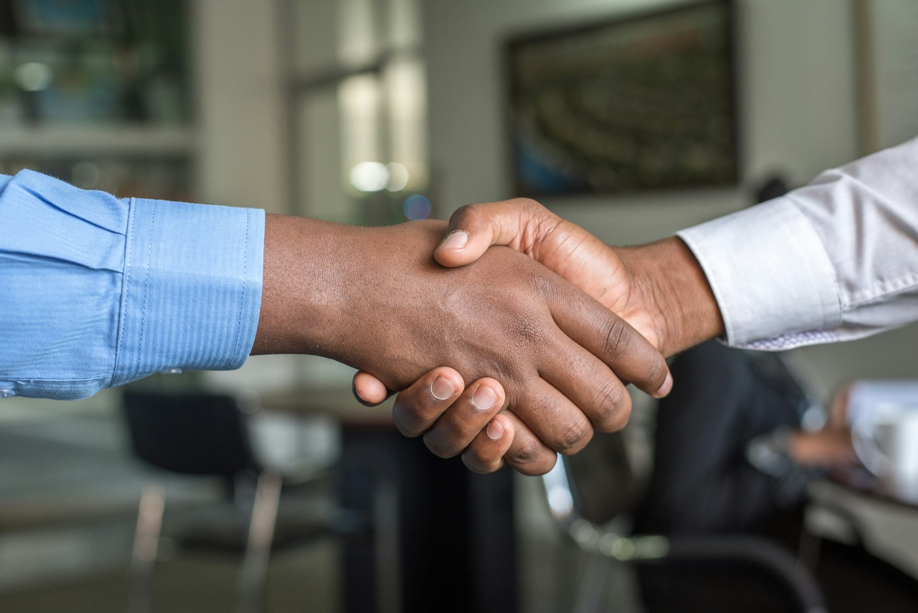 Zwei Personen im Büro reichen sich lachend die Hand